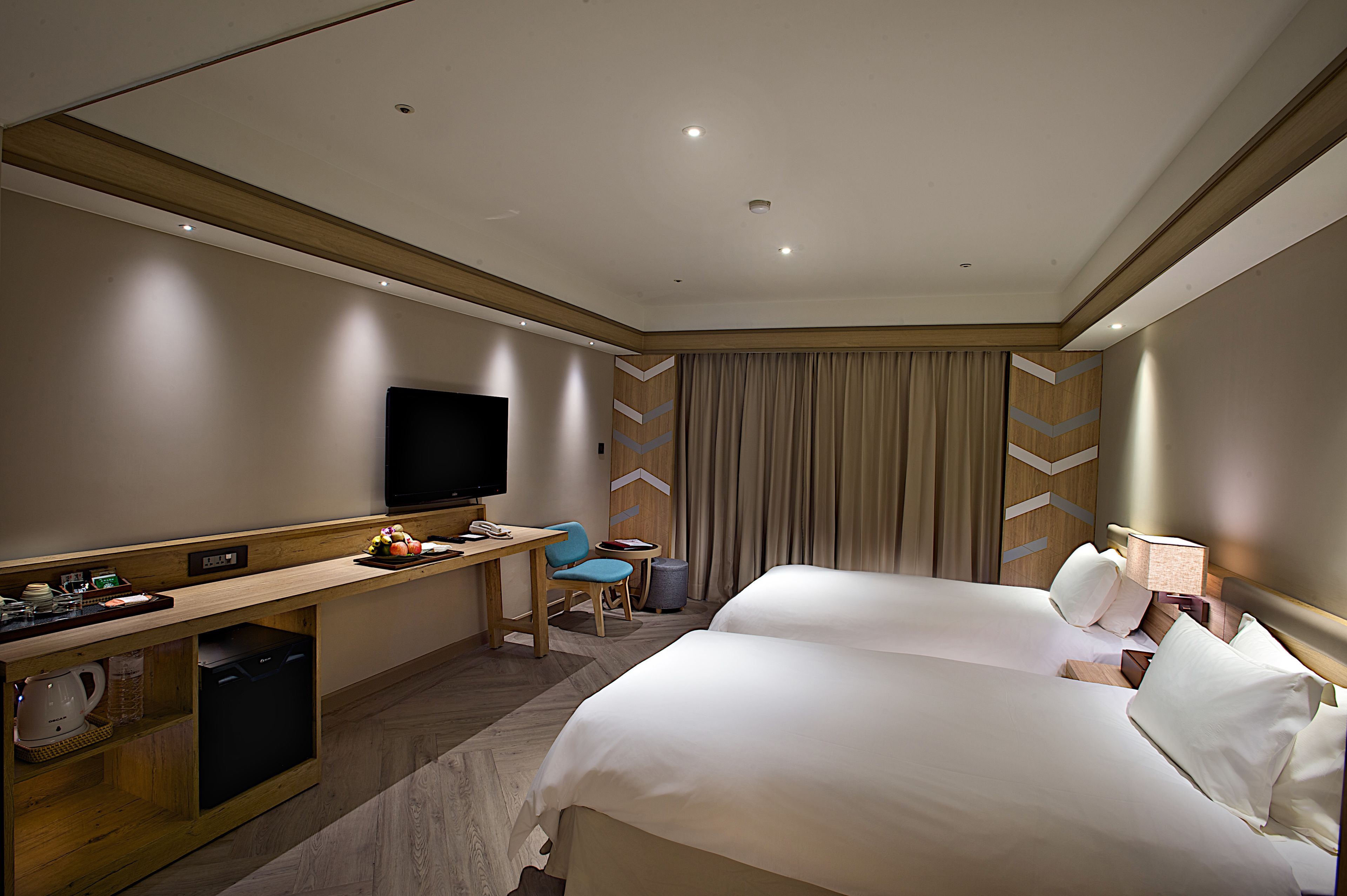 A hotel room with two beds, a desk, a television, and a minibar.