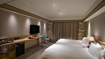 A hotel room with two beds, a desk, a television, and a minibar.