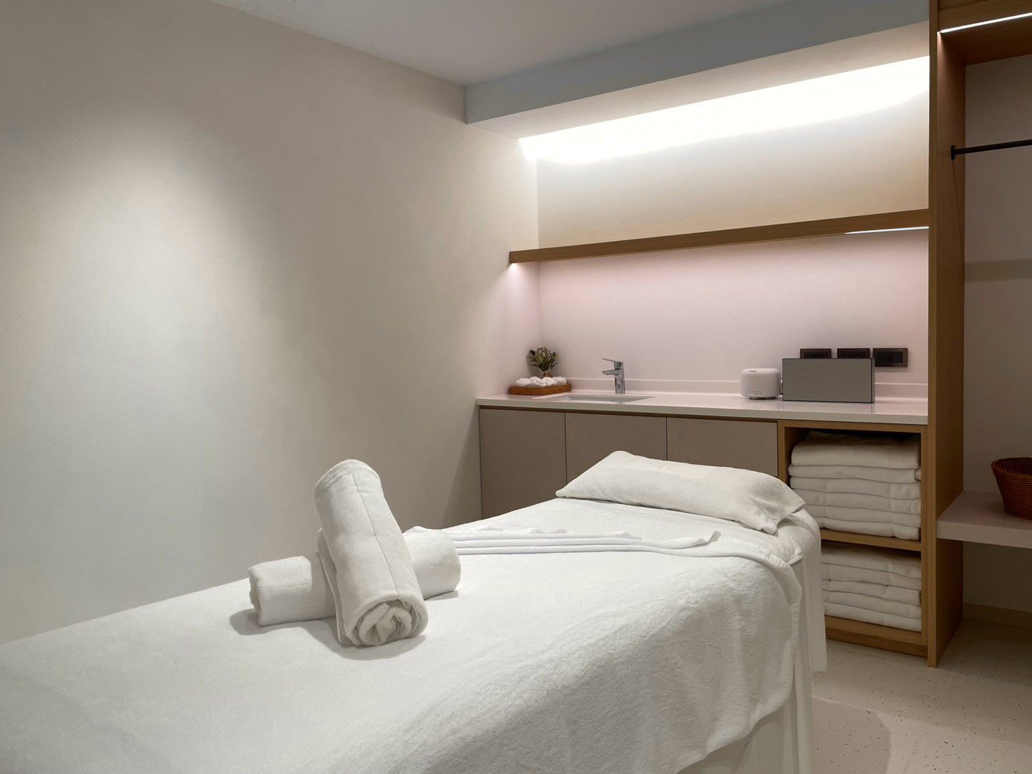 Un baño moderno con cama, lavamanos y repisa con toallas.