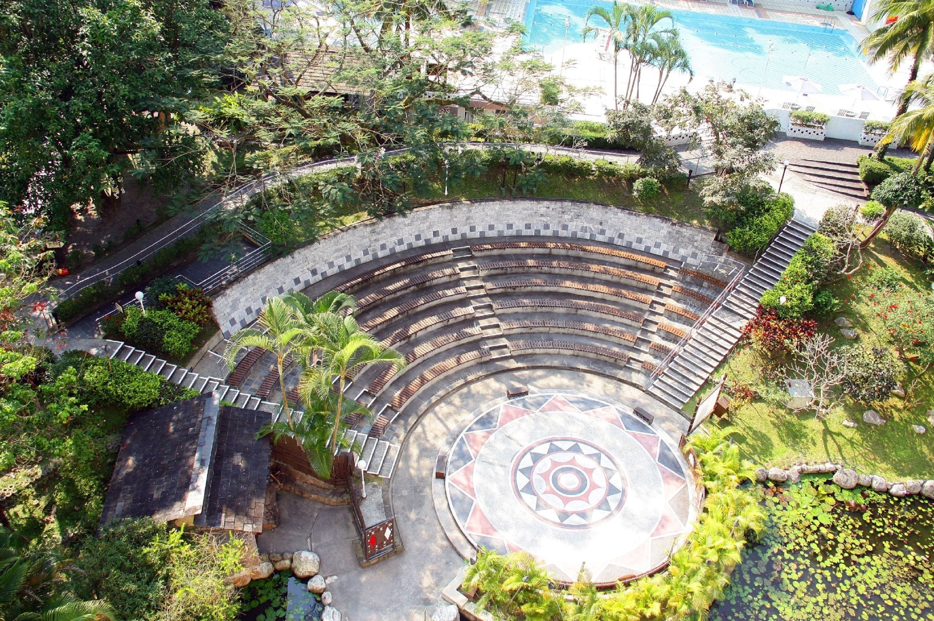 A circular amphitheater with tiered seating, surrounded by lush greenery and a central decorative pattern.