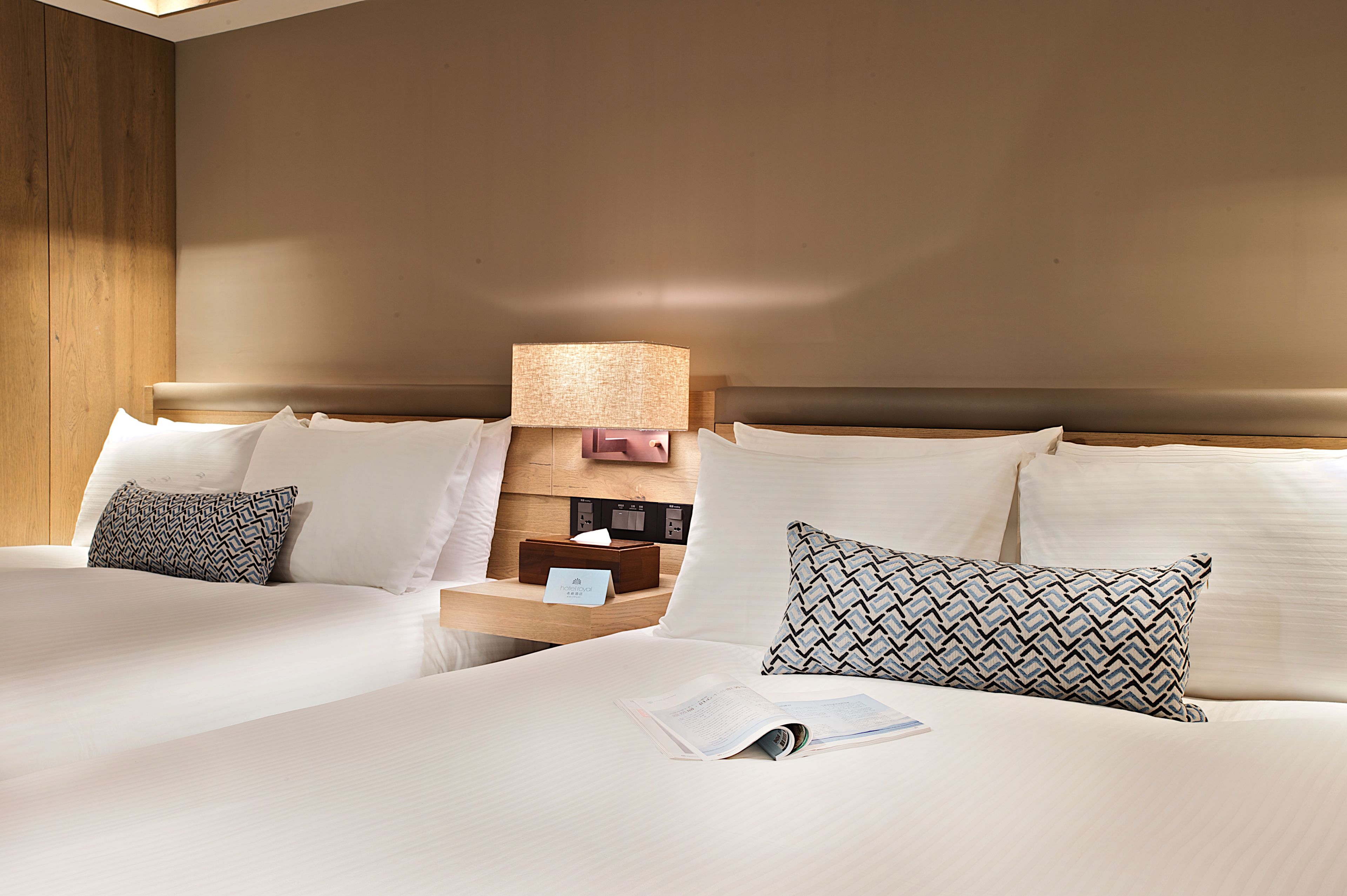 A hotel room with two beds, a nightstand with a lamp, and a wooden headboard.