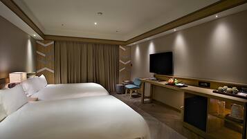 Habitación de hotel con dos camas grandes, un escritorio, un televisor de pantalla plana, una mesita y un minibar.