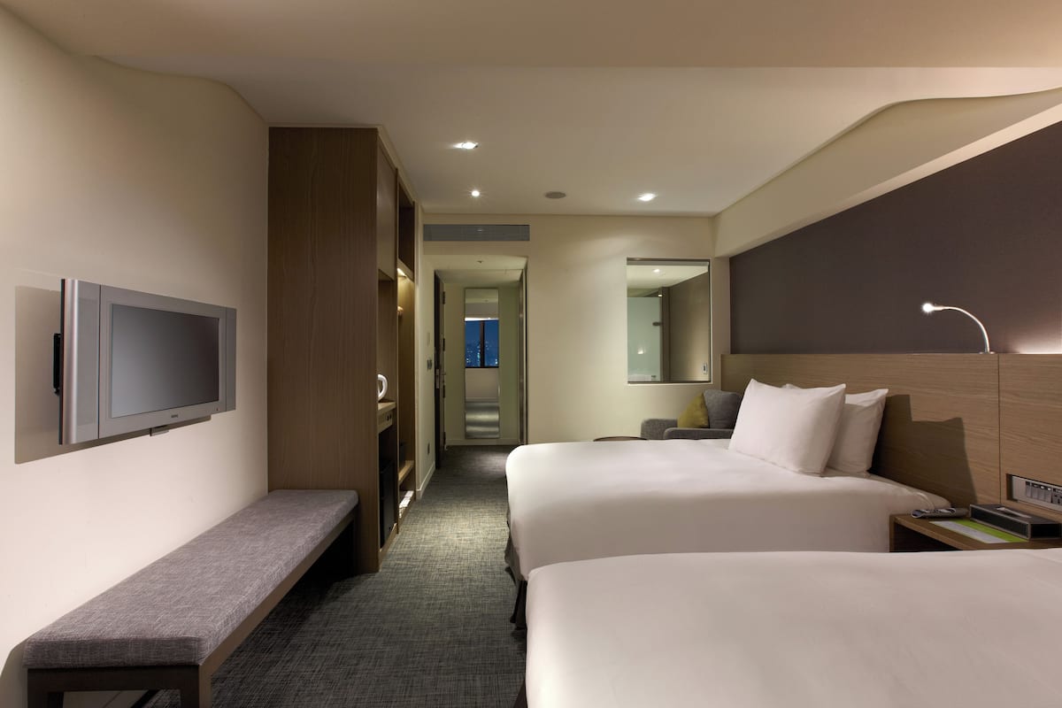 A hotel room with two beds, a bench, a TV, a mirror, and a nightstand.