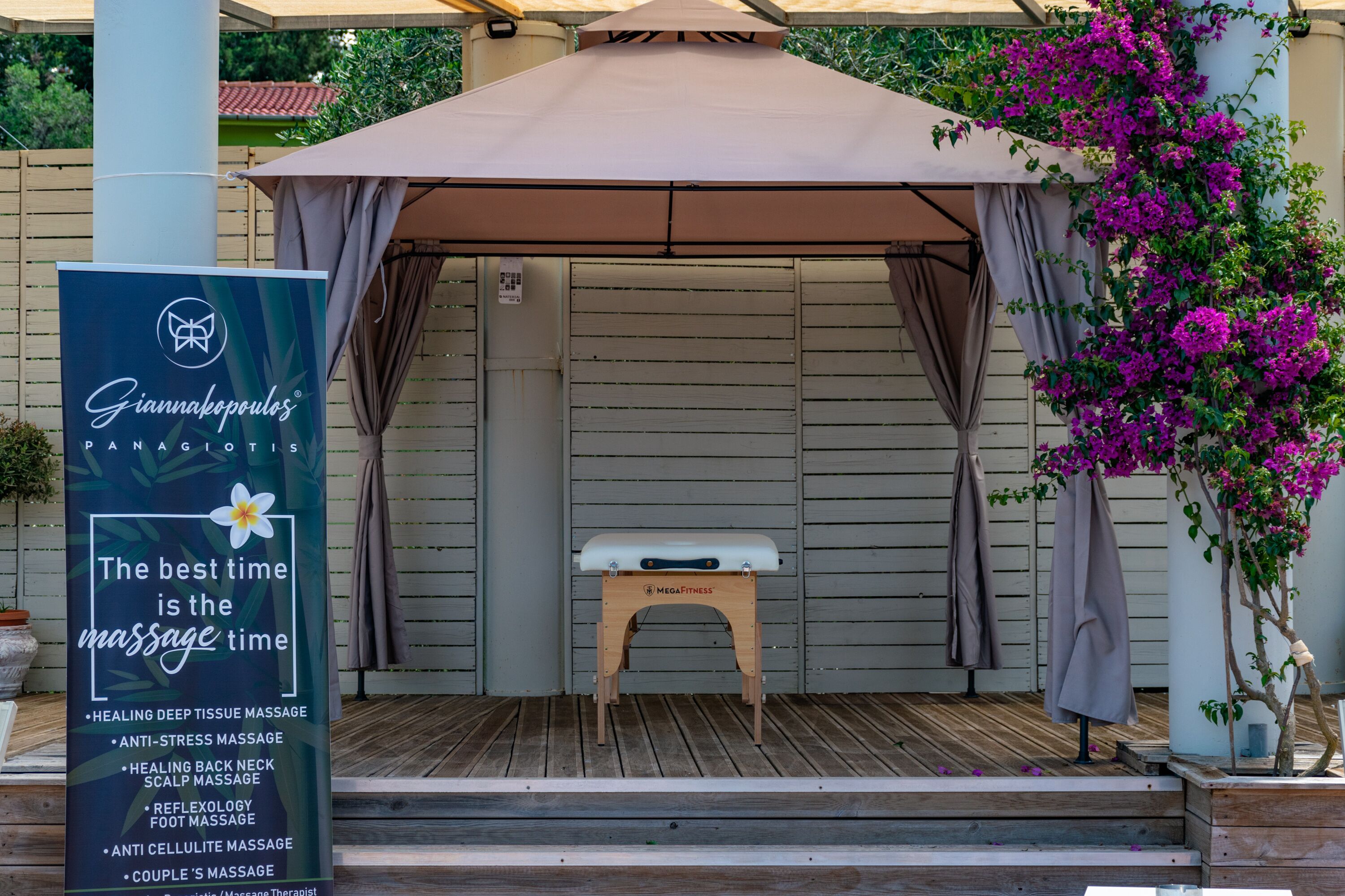 Un espace dédié aux massages, comprenant un banc en bois, un auvent et un panneau indiquant les services proposés.
