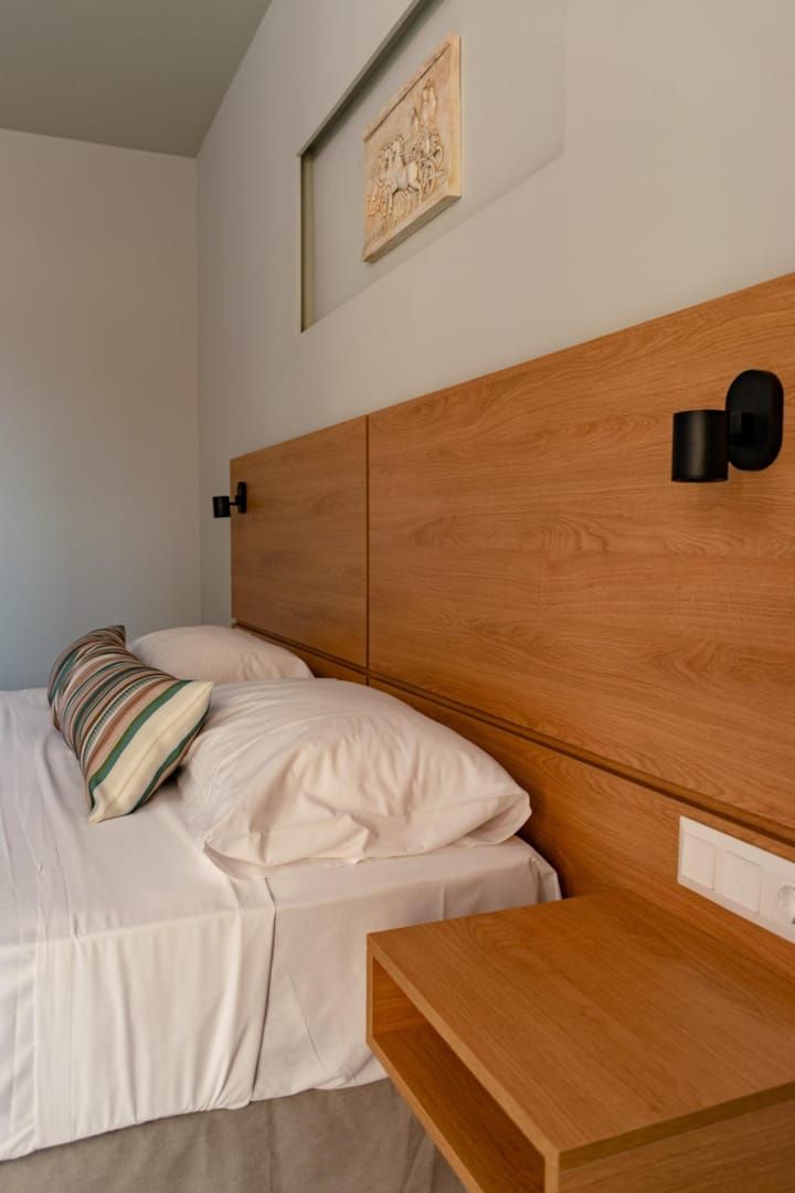 A bedroom with a wooden headboard, a bedside table, and a wall-mounted light fixture.