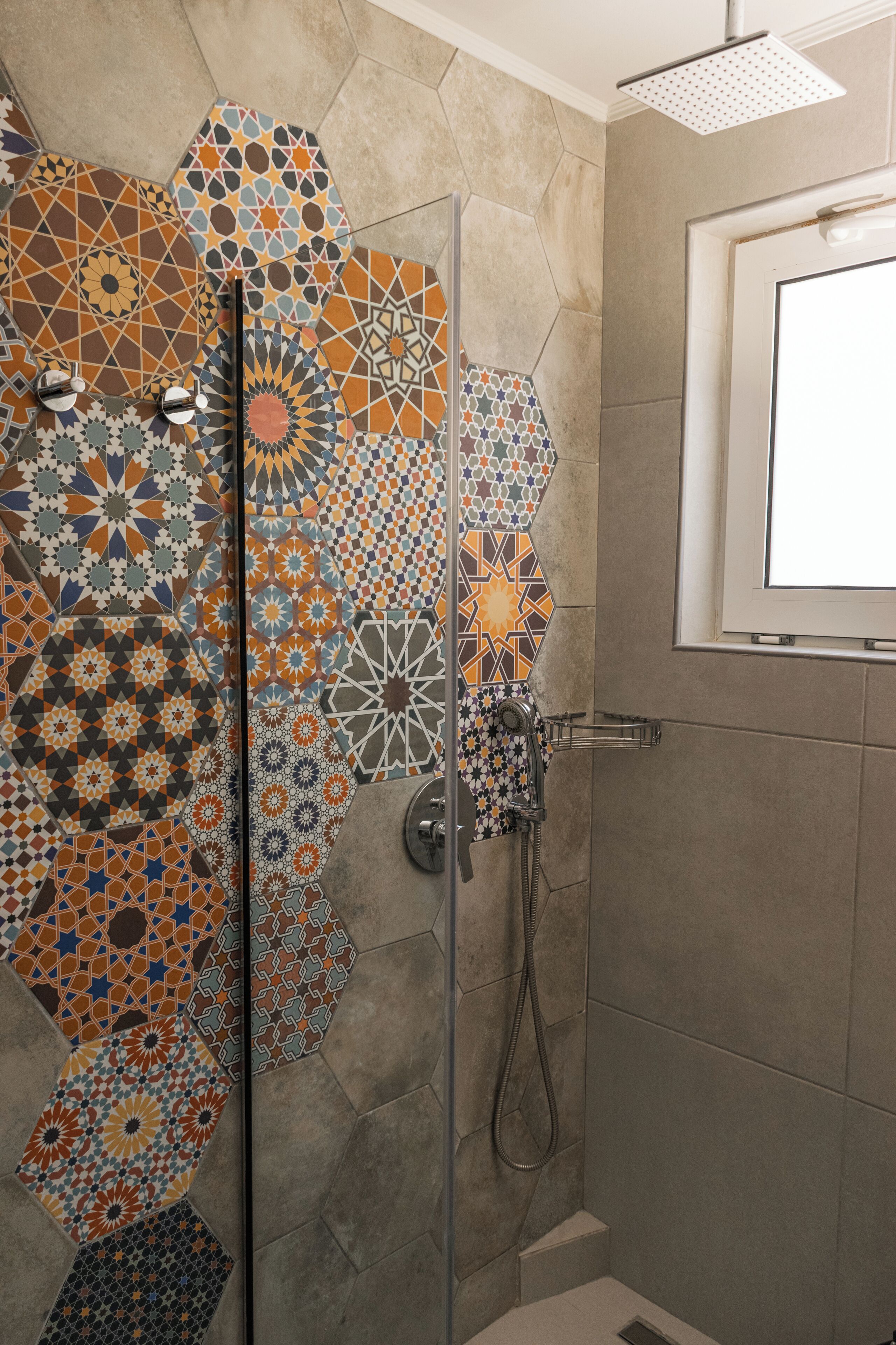 A shower with a glass door and a tiled wall with geometric patterns.