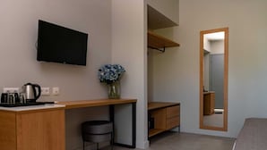 Habitación de hotel moderna con escritorio de madera, televisor de pantalla plana, taburete redondo pequeño y un espejo.
