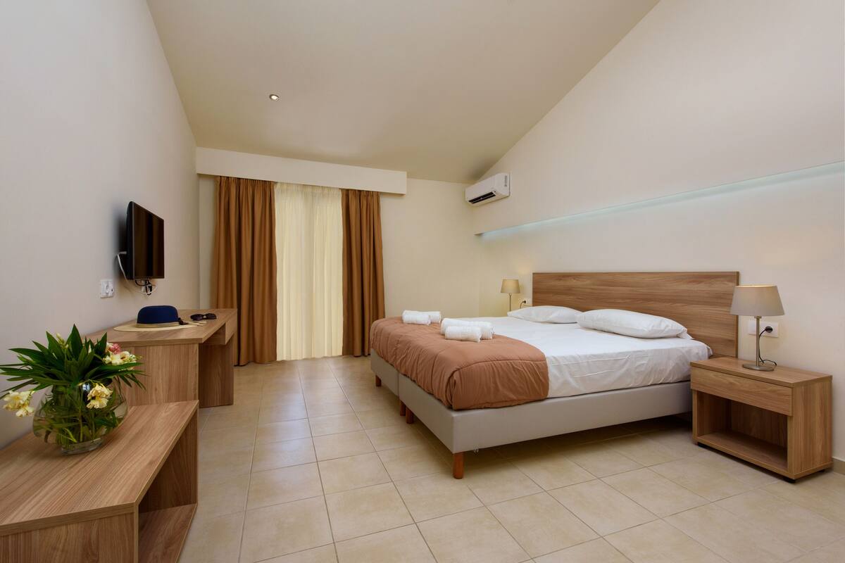 A hotel room with a bed, bedside table, lamp, TV, desk, and curtains.