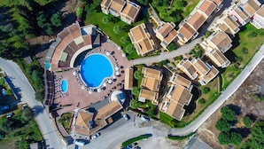 Vista aérea de un resort con una piscina central, varias villas y vegetación circundante.