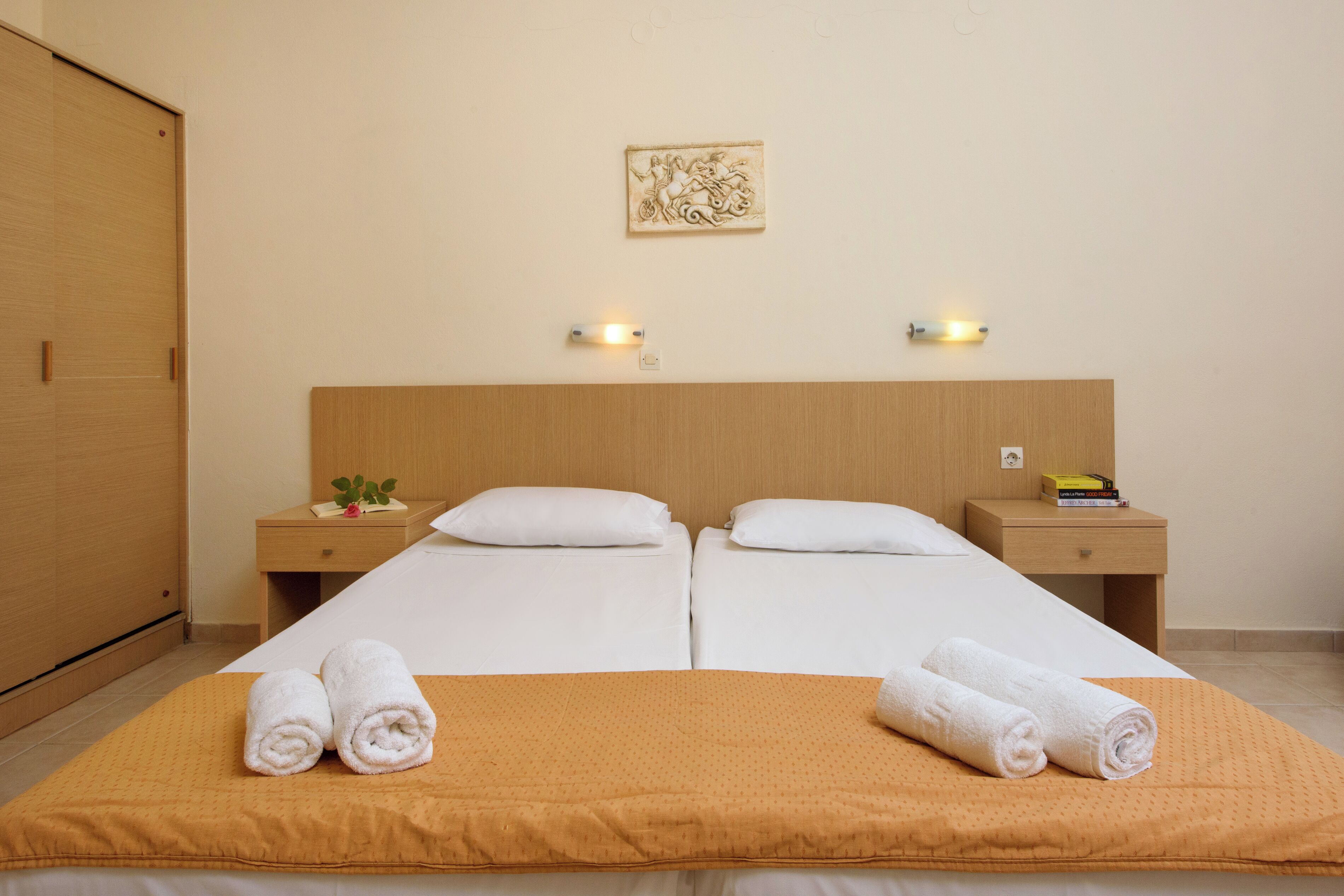 A hotel room with a double bed, two bedside tables, a wooden headboard, and a wall-mounted light fixture.