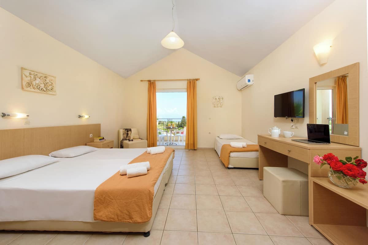 A hotel room with two beds, a desk with a computer, a TV, and a balcony with a view.