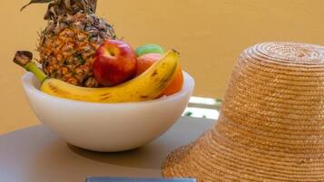 Un saladier rempli de fruits est posé sur une table, à côté d’un chapeau de paille et d’une paire de lunettes de soleil.