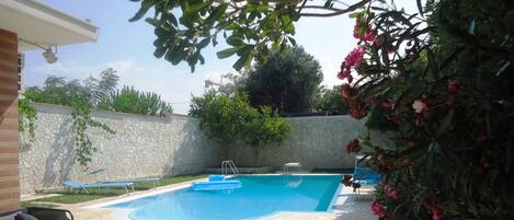 A swimming pool with a stone deck, a lounge chair, and a small table.