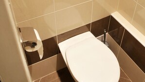 A modern bathroom with a toilet, a shelf with toiletries, and a toilet paper holder. - Apartment Prague City (Prague)