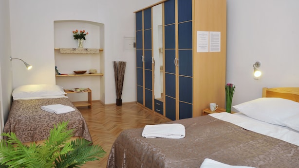 A hotel room with two beds, a wardrobe, a small table with a vase, and a shelf with decorative items. - Apartment Prague City (Prague)
