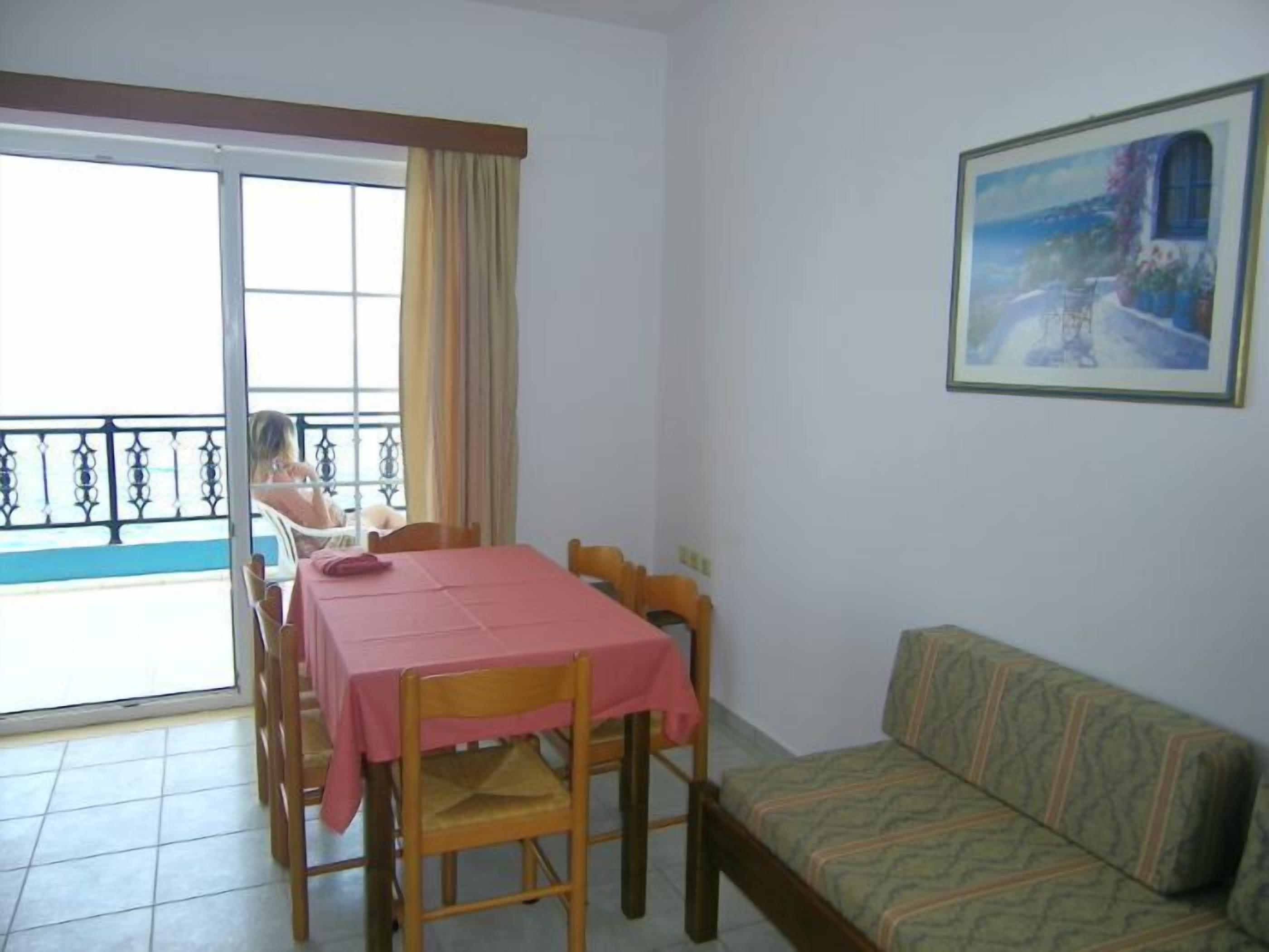 Una habitación con balcón, una mesa de comedor con sillas, un sofá y un cuadro en la pared.
