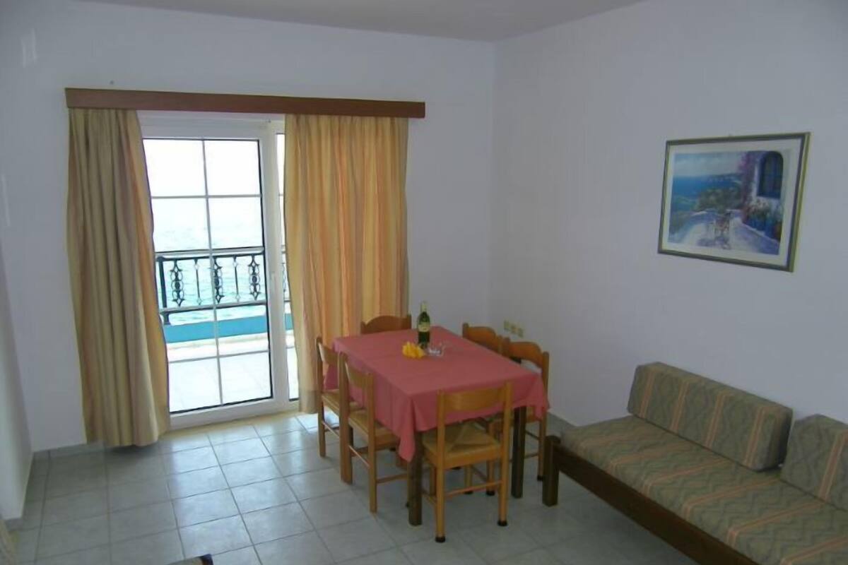 A dining area with a table and chairs, a sofa, a balcony with curtains, and a painting on the wall.