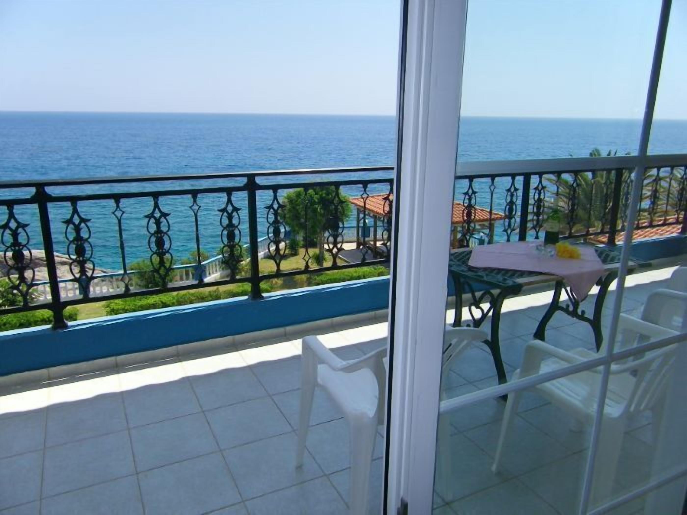 A balcony with a view of the sea, a table with chairs, and a glass door.