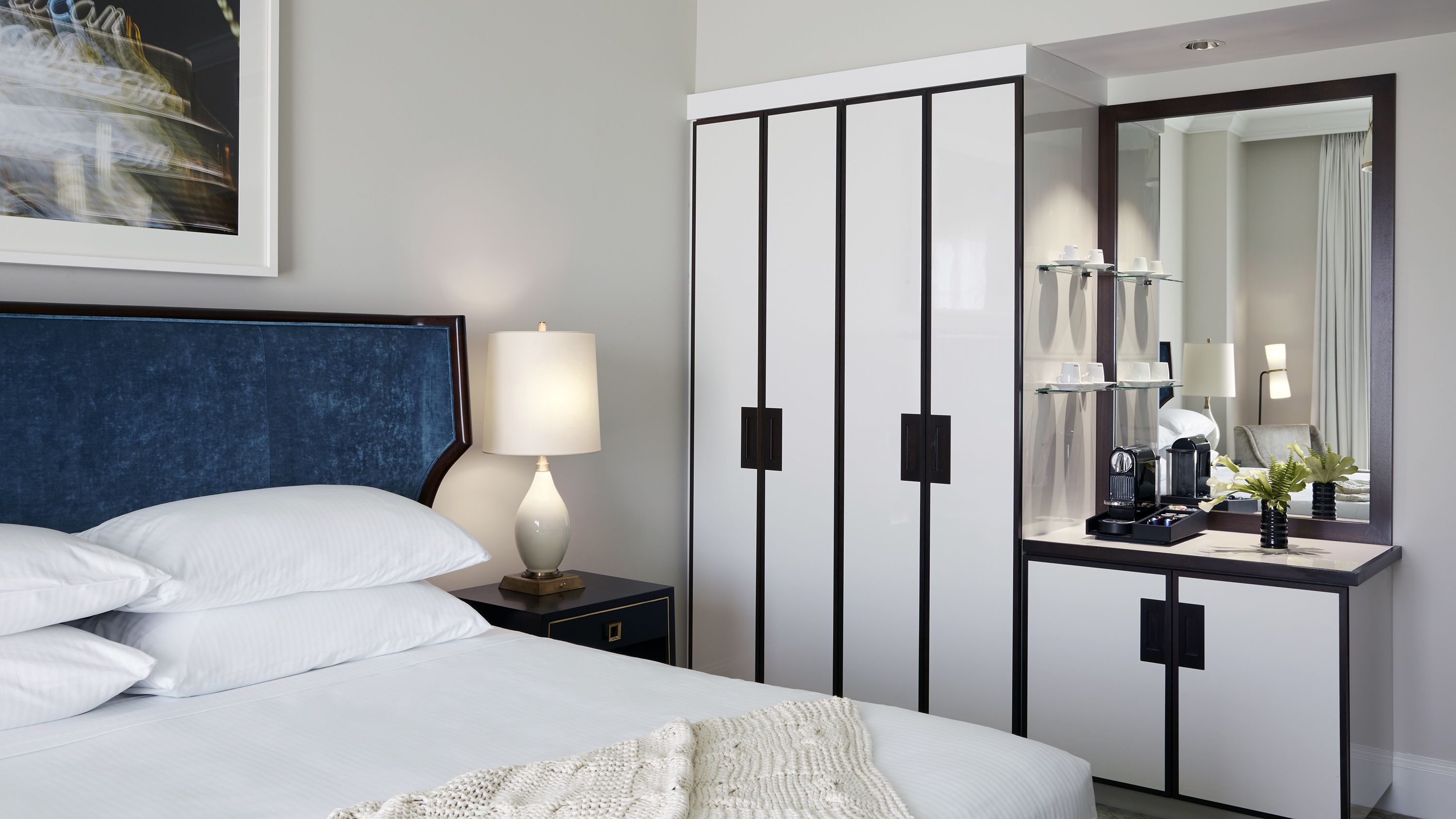 Et pænt og ryddeligt hotelværelse med seng, sengebordlampe, garderobe og spejl.