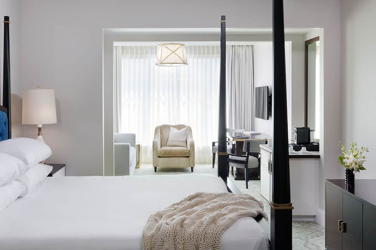 Hotellihuone, jossa on suuri sänky, oleskelualue tuolilla, työpöytä tietokoneella ja peili.