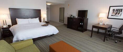 A hotel room with a large bed, a desk with a chair, a television, and a sofa.