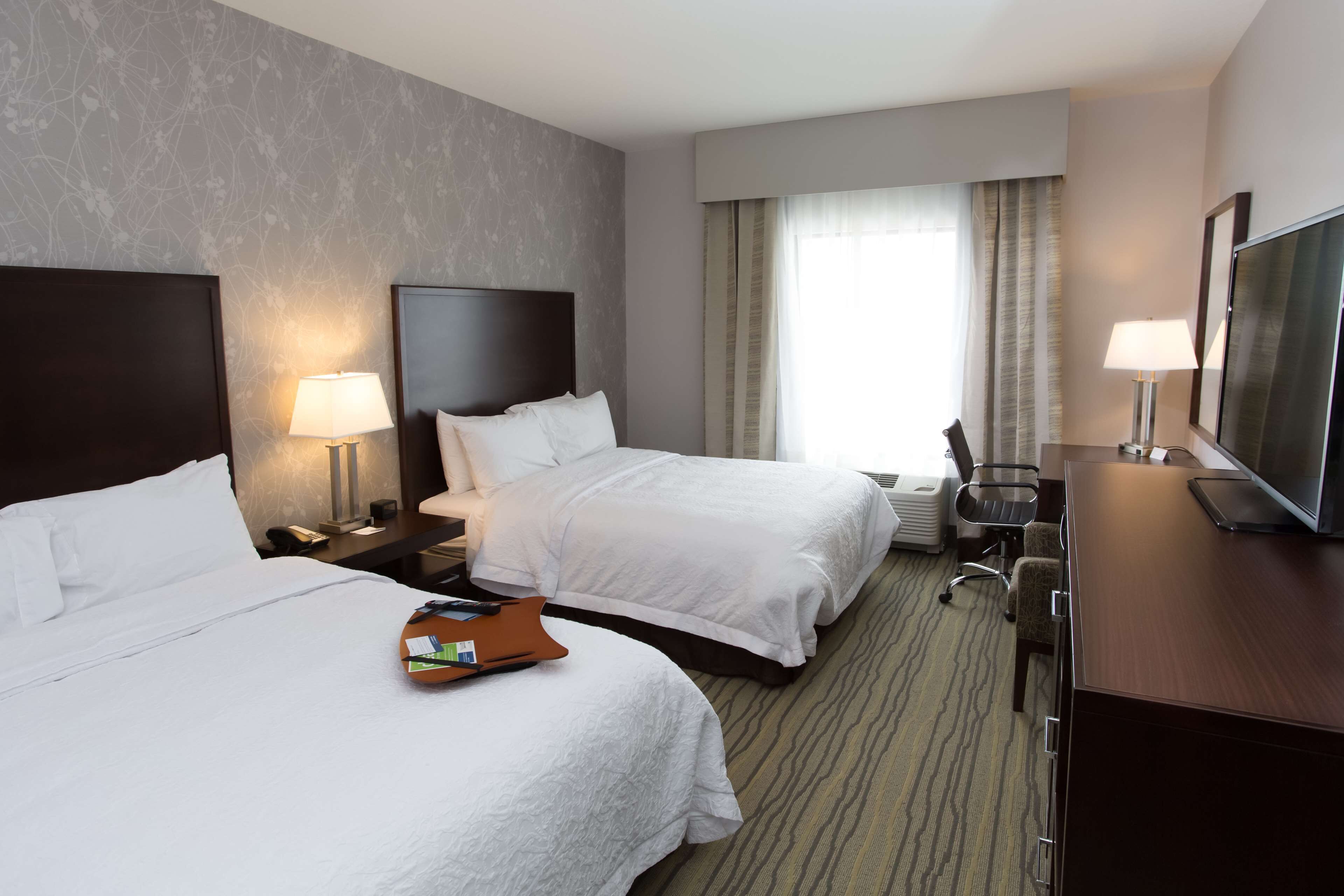 A hotel room with two beds, a desk with a TV, a chair, and a lamp.