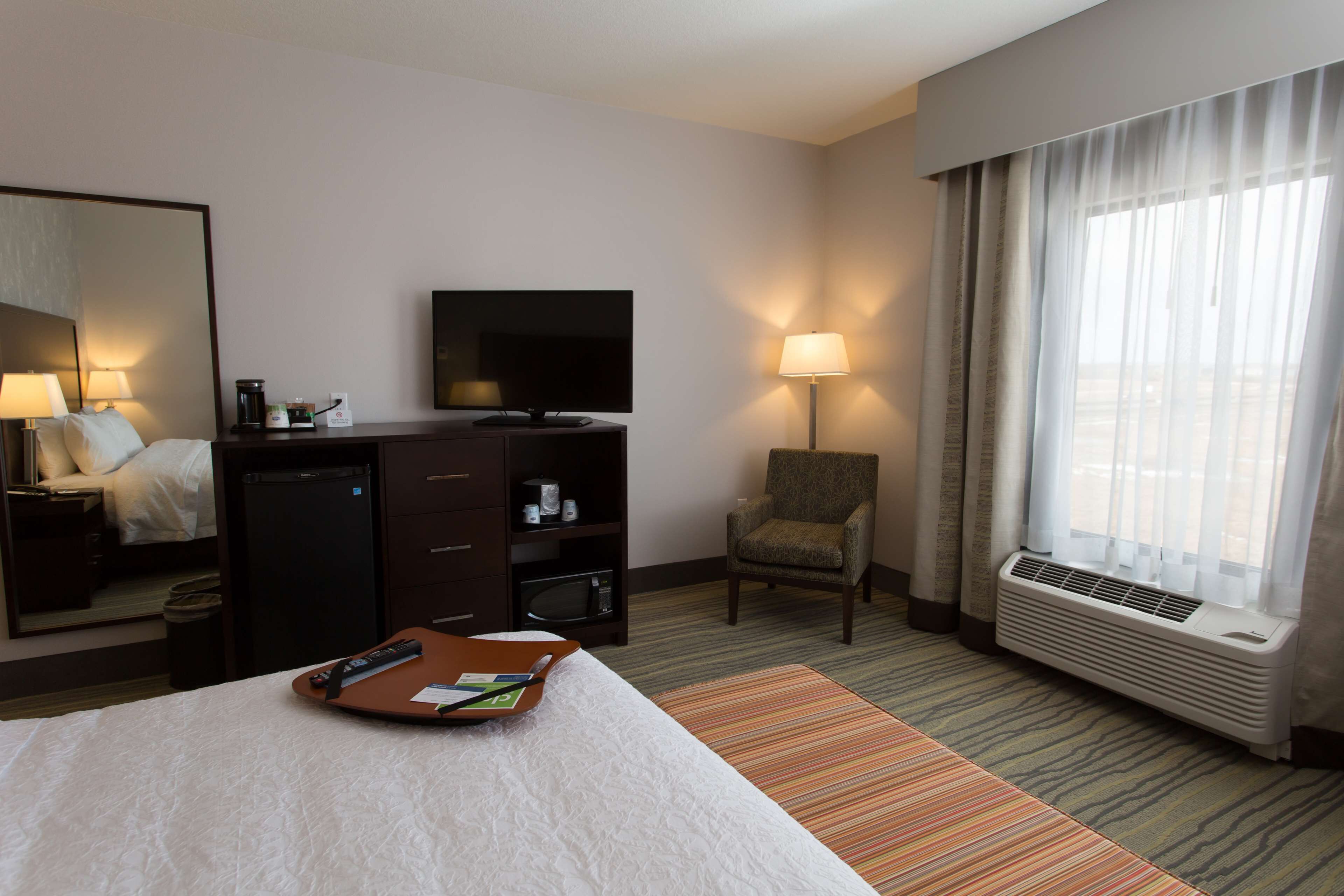 A hotel room with a bed, a desk with a TV, a chair, and a window with curtains.