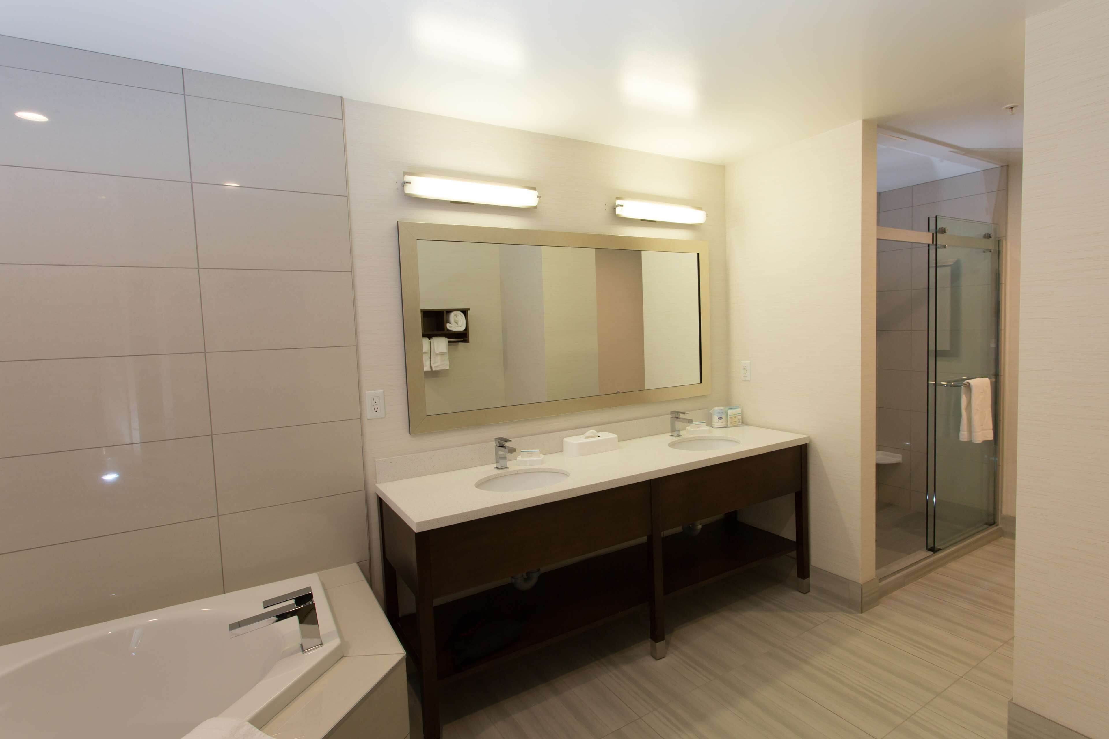 Un baño moderno con un espejo grande, dos lavamanos, una bañera y un box de ducha de vidrio.