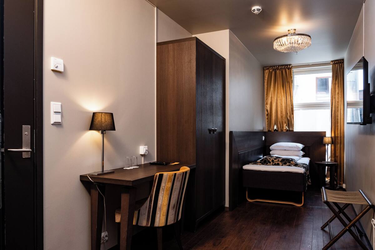 A hotel room with a bed, a desk, a chair, a small table, and a TV.