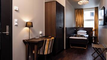 A hotel room with a bed, a desk, a chair, a small table, and a TV.