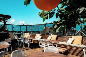 Een terras met houten tafels en stoelen, beklede banken en uitzicht op de stad.