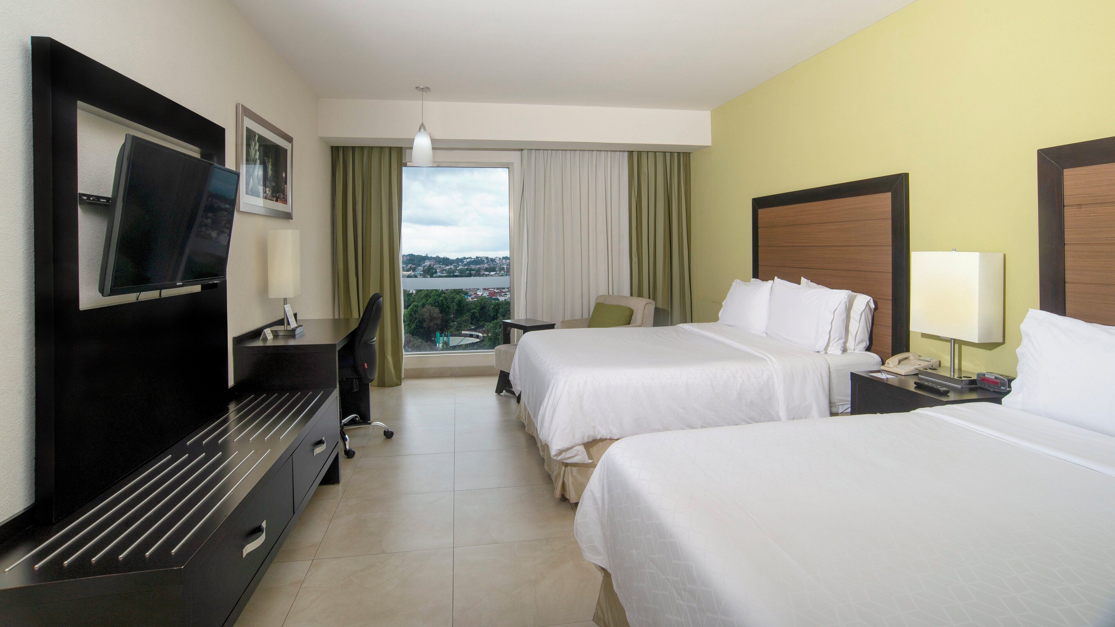 Habitació d'hotel amb dos llits, escriptori, televisió i vista a la ciutat.
