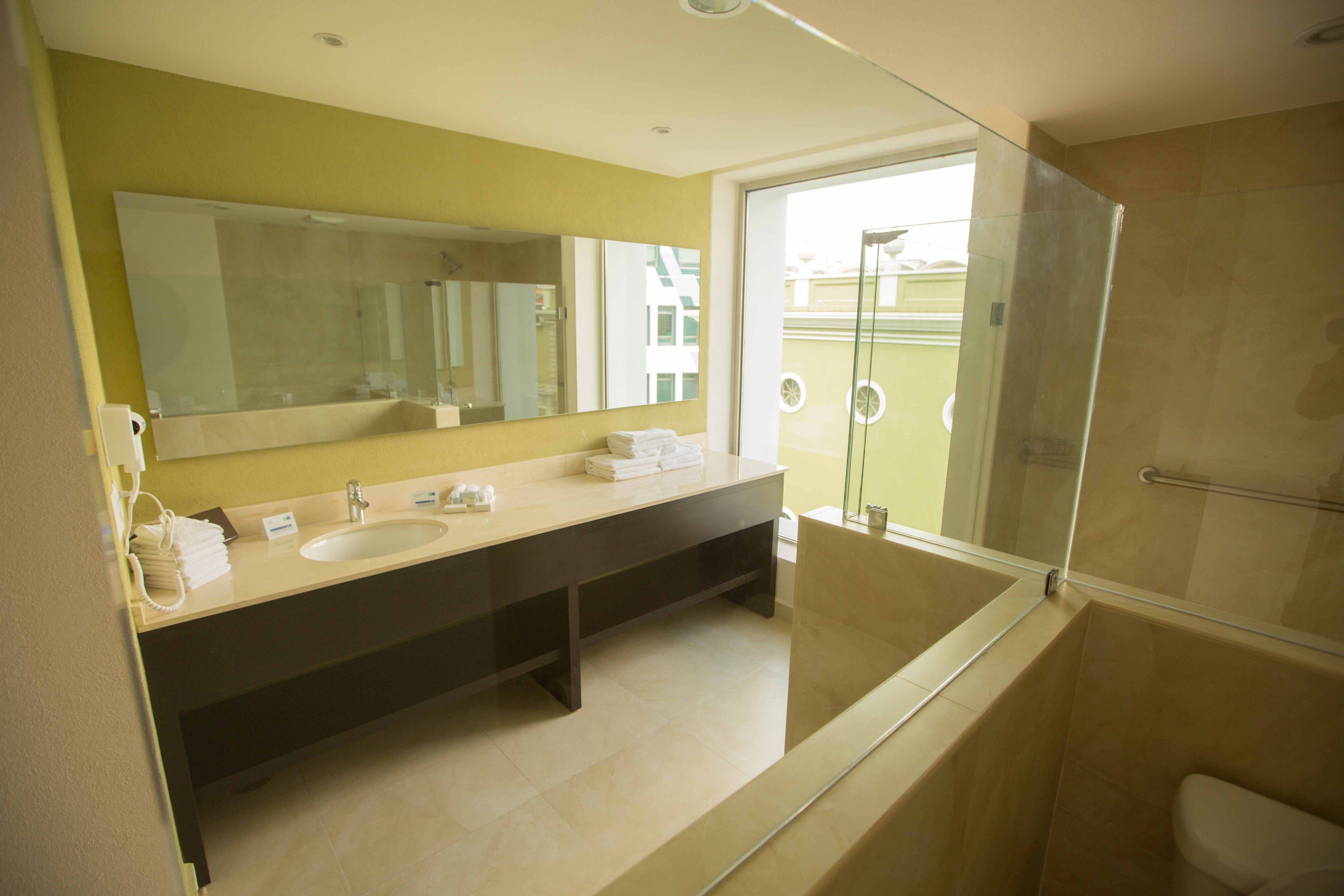 A modern bathroom with a large mirror, two sinks, and a glass-enclosed shower.
