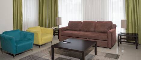 Una sala de estar con un sofá marrón, un sillón amarillo y un sillón azul. En el centro, hay una mesa de centro.