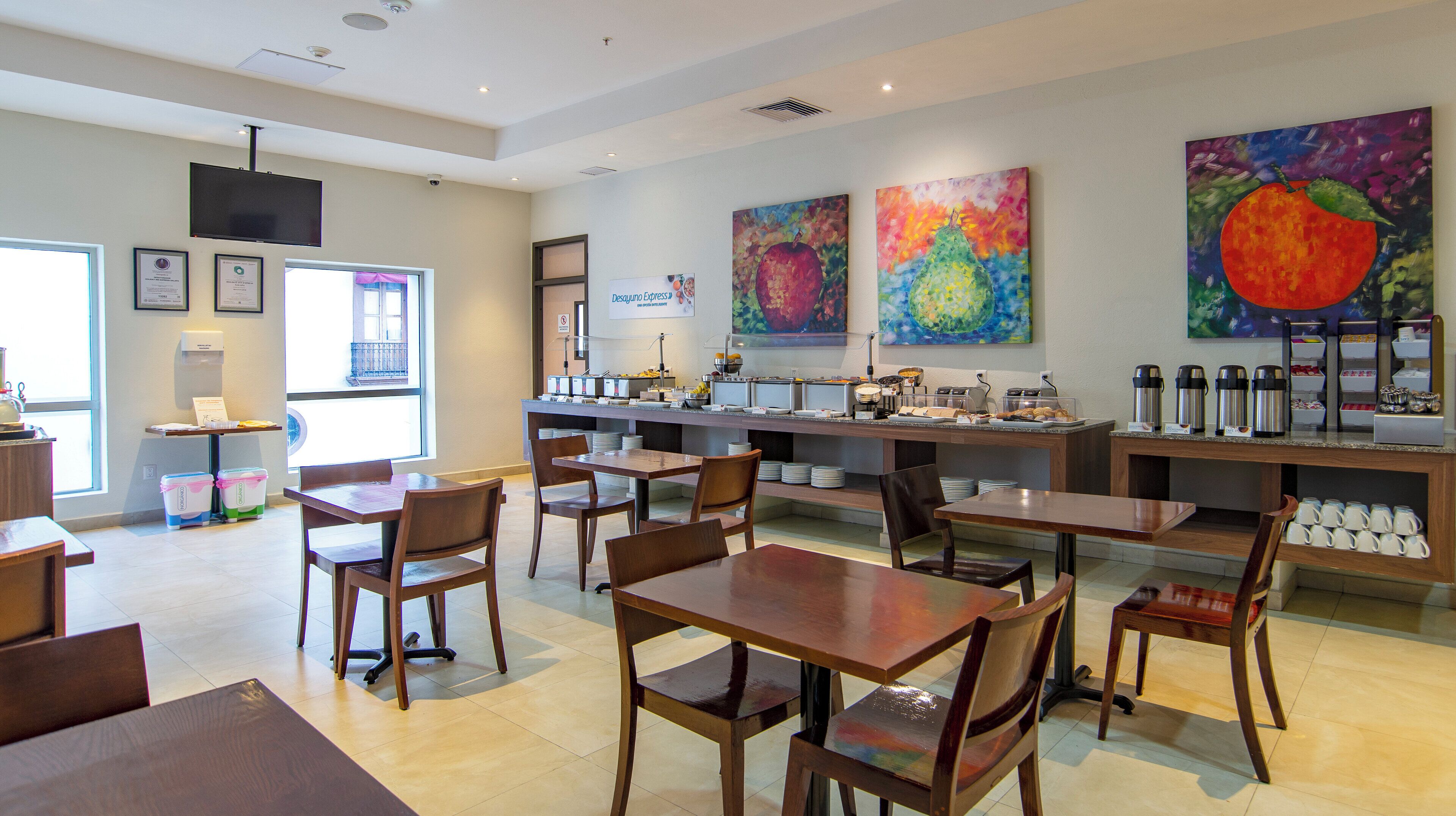 Un restaurante con buffet, mesas de madera, sillas y pinturas coloridas en las paredes.
