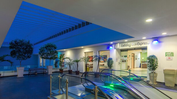 Eine Hotelhalle mit einer Rolltreppe, Topfpflanzen und einem Schild von Holiday Inn Express.