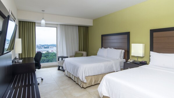 Quarto de hotel com duas camas, uma mesa, uma cadeira e vista para a cidade através da janela.