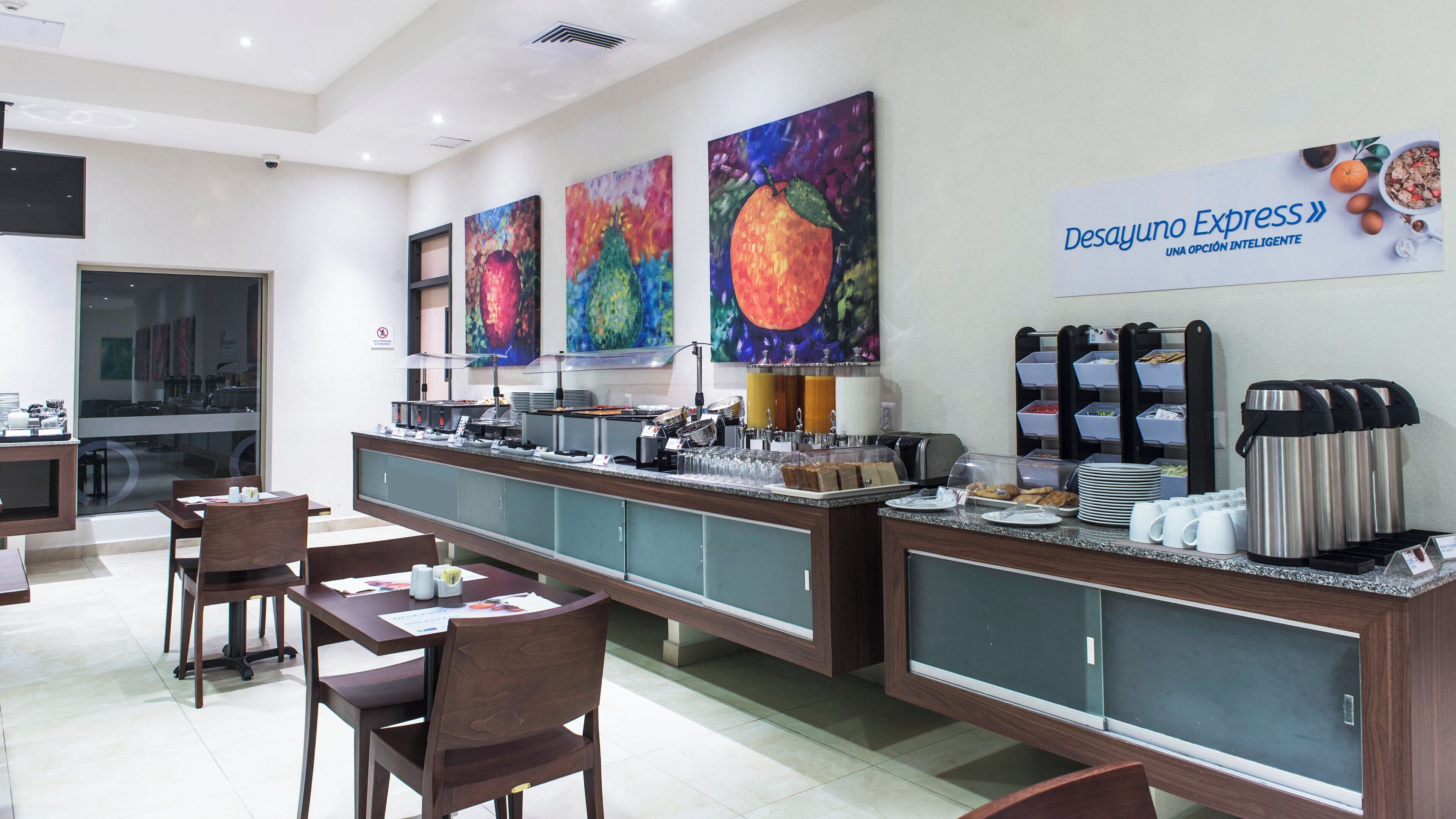 A hotel breakfast area with a buffet counter, seating, and artwork on the walls.
