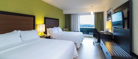 A hotel room with two beds, a desk, a chair, a TV, and a window with a view.