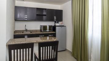 A compact kitchen with dark cabinets, a microwave, a refrigerator, a sink, and two chairs.