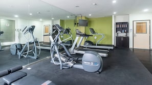 A gym with treadmills, ellipticals, and a mirrored wall.