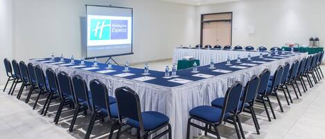 Una sala de conferencias con una larga mesa, sillas, una pantalla de proyector y el logotipo de Holiday Inn Express.
