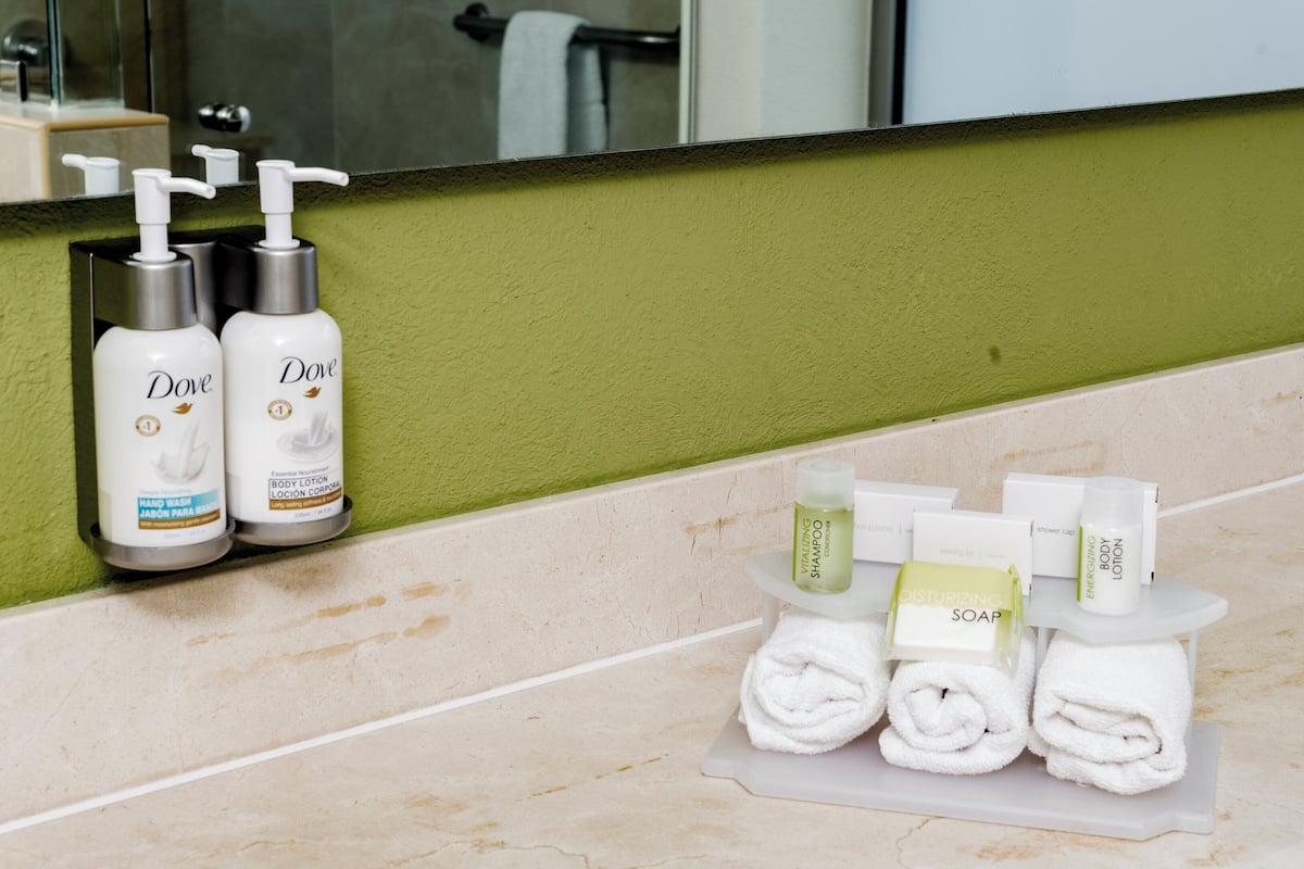 A bathroom counter with Dove body lotion and hand wash, a shower cap, and towels.