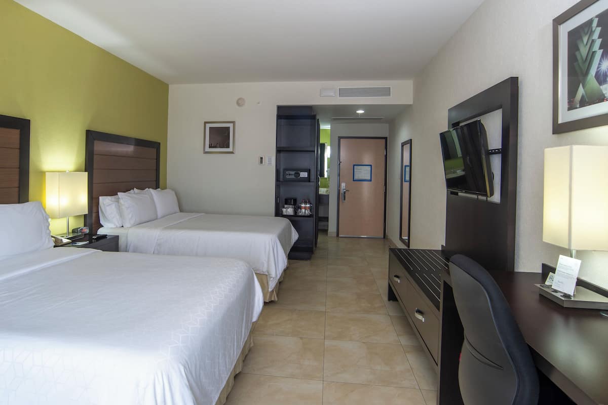 A hotel room with two beds, a desk with a computer, a TV, and a minibar.