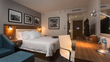 A hotel room with a bed, a desk, a chair, a TV, and framed pictures on the wall.