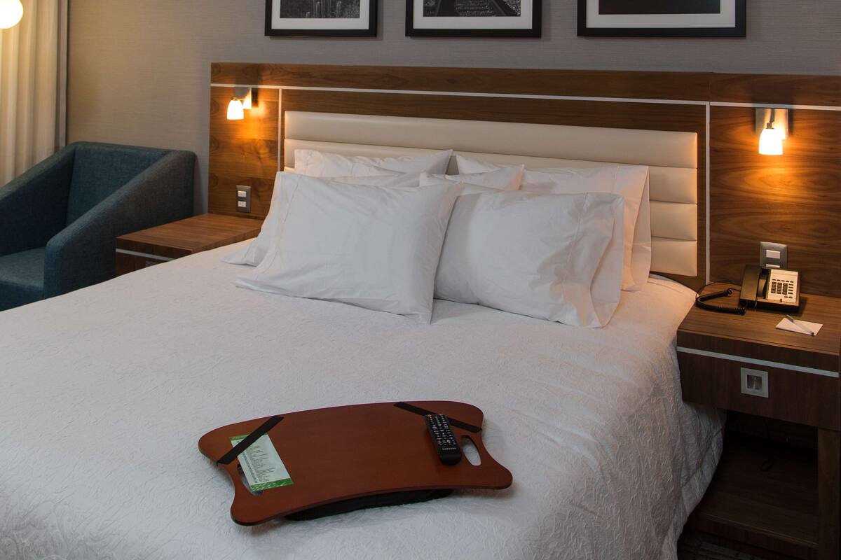 Habitación de hotel con una cama grande, dos mesitas de noche con lámparas, una silla y tres cuadros en la pared.