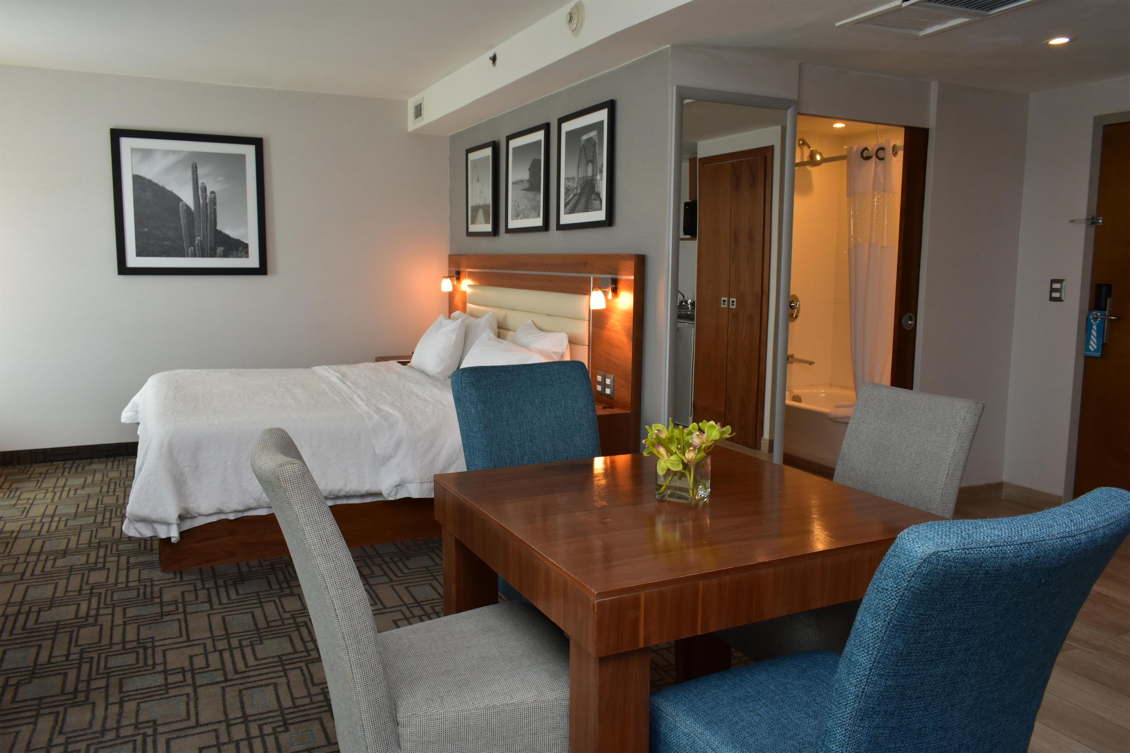 Una habitación de hotel con una cama, una mesa de madera, dos sillas y un pequeño florero con flores.