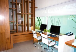 A modern office with two desks, computers, and office chairs. There is a wooden bookshelf with decorative items and a large window with a view of greenery. - Hampton Inn by Hilton Hermosillo (Hermosillo)