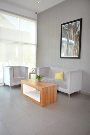 A modern living room with a light grey sofa, a wooden coffee table, and a large window providing natural light. - Hampton Inn by Hilton Hermosillo (Hermosillo)