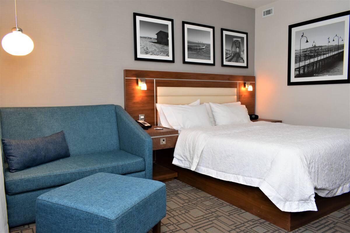 Habitación de hotel con una cama, un sofá azul y una mesita de noche. Hay cuadros enmarcados en la pared sobre la cama.